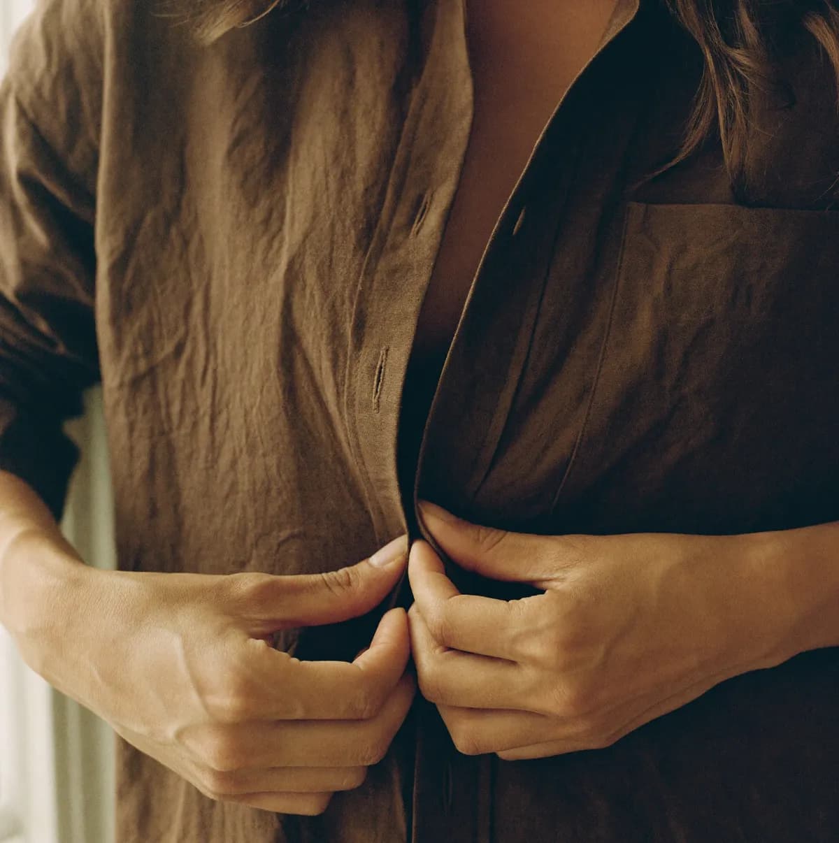 Close-up of hands buttoning a cocoa linen shirt